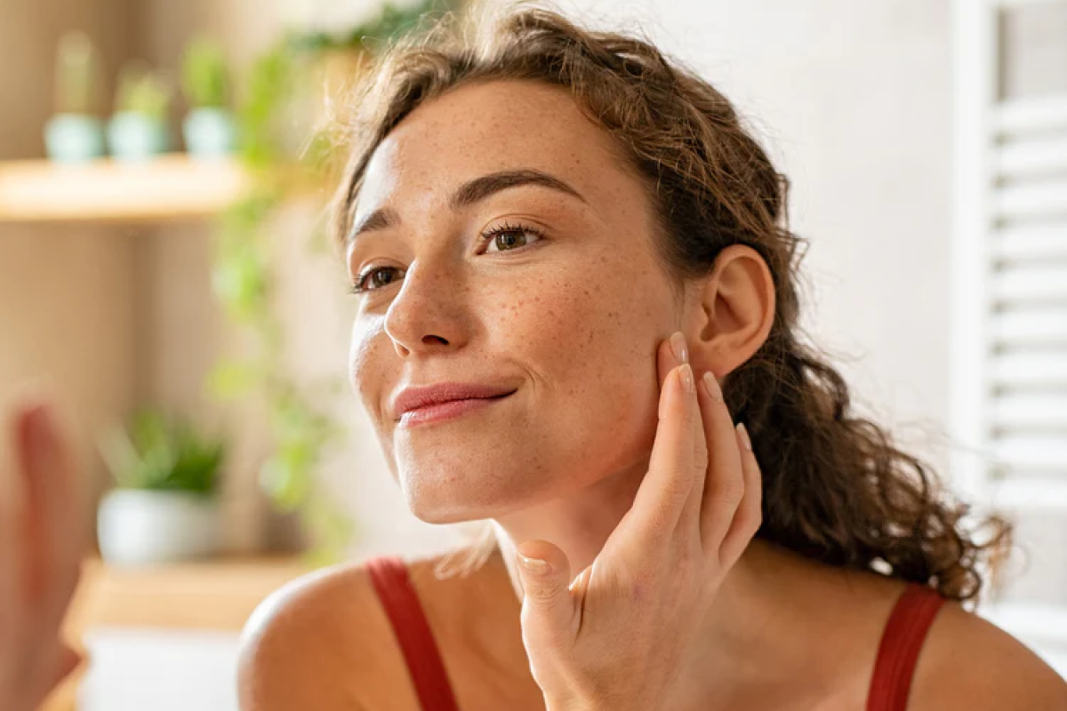 Young woman smiling and touching her face in a bright room.