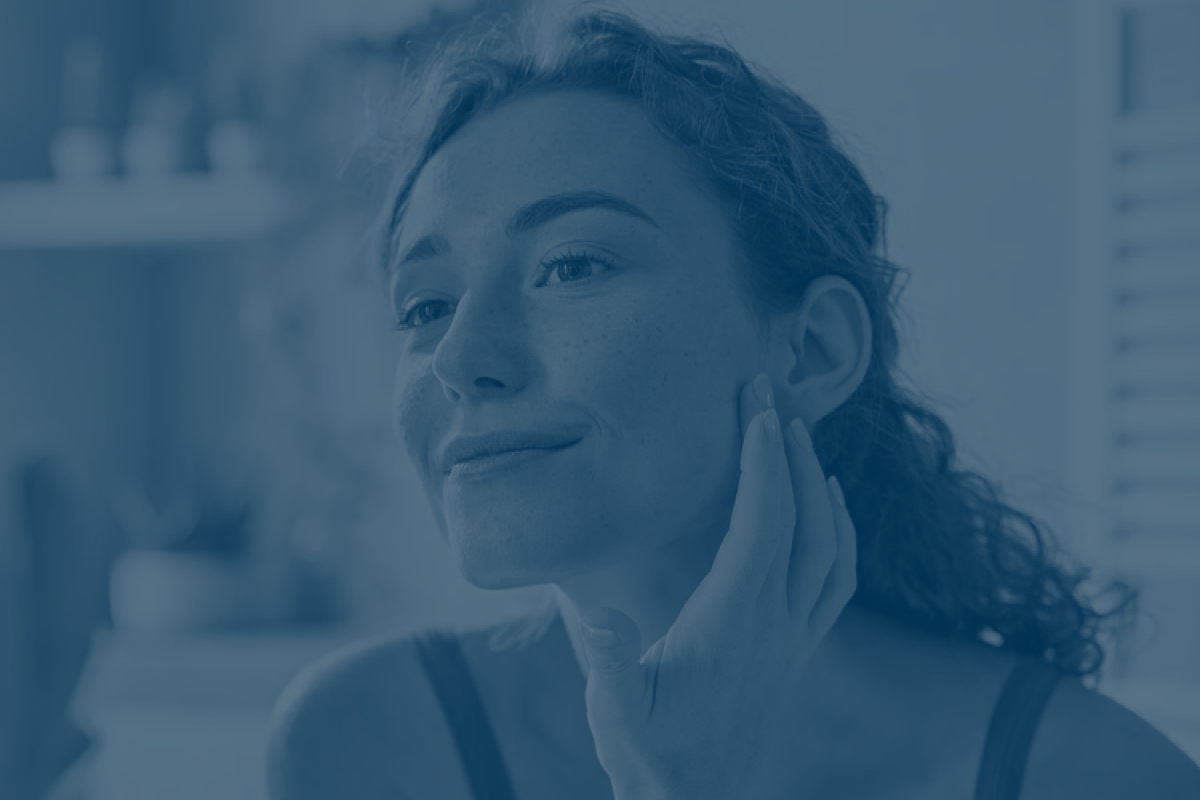 Person gently touching face, looking in mirror, indoors.