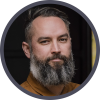 Ross Featherstone. Bearded man with short hair, wearing a brown shirt, neutral expression.